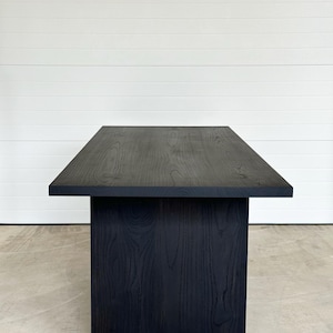 May include: A black wooden dining table with a rectangular top and a single base. The table has a natural wood grain pattern and a smooth, polished finish.