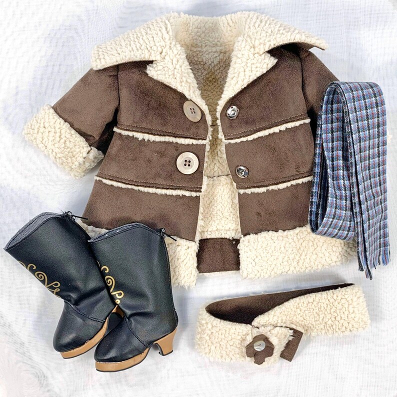 May include: A brown faux suede jacket with a white sherpa lining, a matching brown sherpa collar, and three brown buttons. The jacket is paired with a black leather boot with a gold design, a brown sherpa headband with a button, and a blue and white plaid scarf.