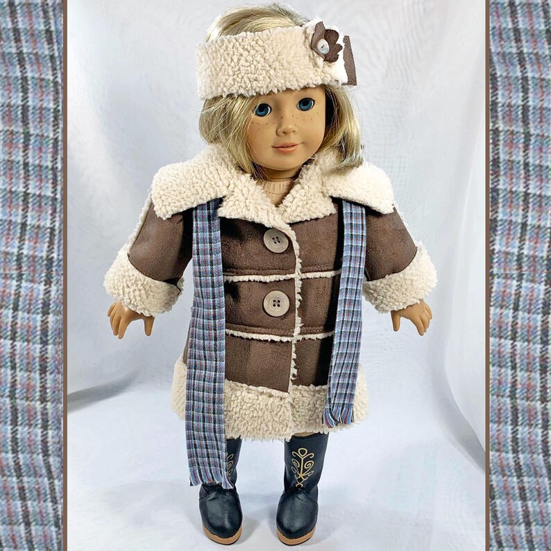 May include: A brown faux fur coat with a white faux fur collar and cuffs. The coat has a plaid scarf and a white headband with a brown flower accent. The doll is wearing black boots.