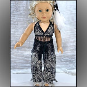May include: A doll wearing a black and white paisley print outfit. The outfit includes a halter top with fringe and matching wide-leg pants. The doll has blonde hair and is wearing a feather hair accessory. The doll's outfit is a bohemian style.