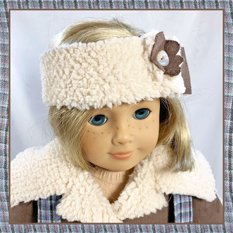 May include: A doll wearing a white faux fur headband with a brown flower accent and a white faux fur collar on a brown jacket.
