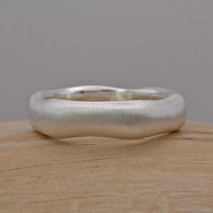 Op de afbeelding: Een zilveren ring met een glad, afgerond en licht golvend oppervlak. De ring heeft een geborstelde afwerking.