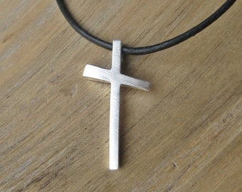 May include: A silver cross pendant on a black leather cord necklace.
