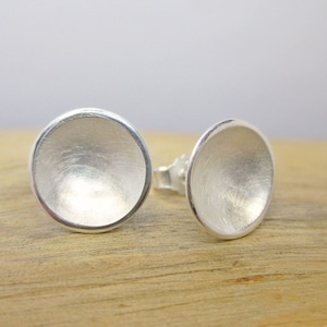 Può includere: Un paio di orecchini a bottone in argento con un design rotondo leggermente concavo. Gli orecchini hanno una finitura spazzolata.