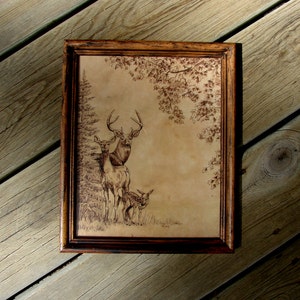 May include: A framed wood-burned image of a deer family in a forest setting. The image is on a light brown background with a dark brown frame.