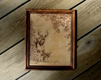May include: A framed wood-burned image of a deer family in a forest setting. The image is on a light brown background with a dark brown frame.