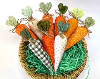 May include: A basket filled with green grass and nine handmade fabric carrots. The carrots are in various shades of orange and green with white polka dots.