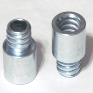 May include: Two cylindrical metal adapters with a silver finish. Each piece features a smooth base section and a threaded top section designed for connecting components. The metal has a reflective surface and a uniform industrial appearance.