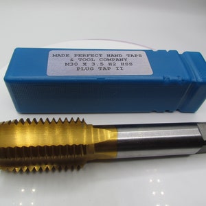 Può includere: Un maschio per filetti dorato con una custodia in plastica blu. La custodia ha un'etichetta che recita "MADE PERFECT HAND TAPS & TOOL COMPANY M30 X 3.5 H2 HSS PLUG TAP II".
