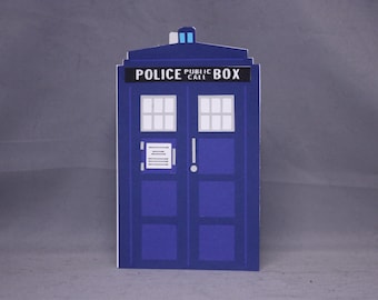 May include: A blue cardboard cutout of a police public call box. The box has a white door with a small window and a sign that reads "Police Public Call Box".