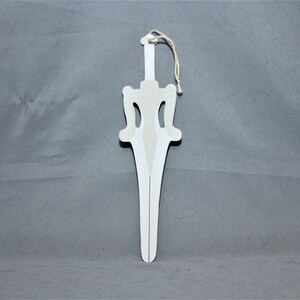May include: A white paper sword ornament with a string loop for hanging. The sword has a pointed tip and a decorative design on the handle.