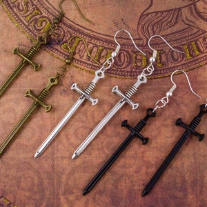 May include: Four pairs of sword earrings in silver, gold, and black. The earrings are dangling and feature a sword design.