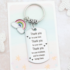 May include: Silver keyring with a rainbow and cloud charm. The keyring has a dog tag pendant with the words "Thank you for your love. Thank you for your care. Thank you for your kindness, and for always being there."