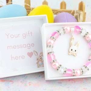 May include: A white gift box containing a pink and white bunny charm bracelet. The box features a pink and white bunny design and the text "Your gift message here" on the front.
