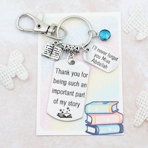 May include: A silver keychain with a book charm, a blue crystal charm, and two silver tags. The tags have the text "I'll never forget you Miss Abdullah" and "Thank you for being such an important part of my story" with a book and stars graphic.