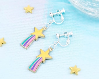 May include: A pair of gold star shooting star clip-on earrings with a pink, blue and yellow striped tail. The earrings are on a light blue background.
