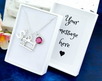 May include: A silver necklace with a sewing machine charm, a letter 'S' charm, and a pink crystal charm. The necklace is in a white gift box with a blank card that says "Your message here".