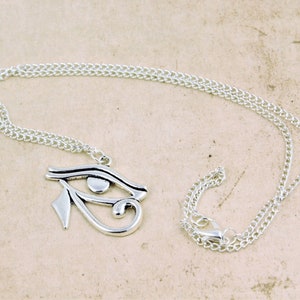 May include: Silver chain necklace with a silver pendant featuring the Eye of Horus symbol.