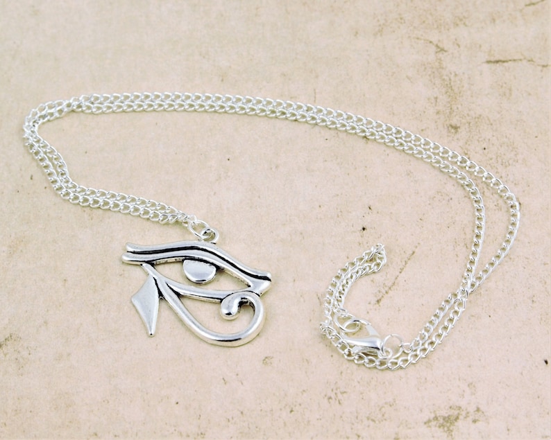 May include: Silver chain necklace with a silver pendant featuring the Eye of Horus symbol.