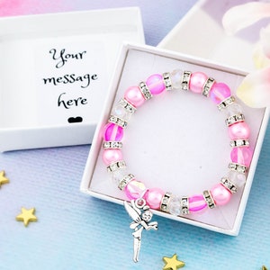 May include: A pink and white beaded bracelet with a silver fairy charm. The bracelet is in a white gift box with the text "Your message here".