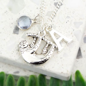 May include: Silver necklace with a sloth charm, a crystal charm, and a letter A charm.