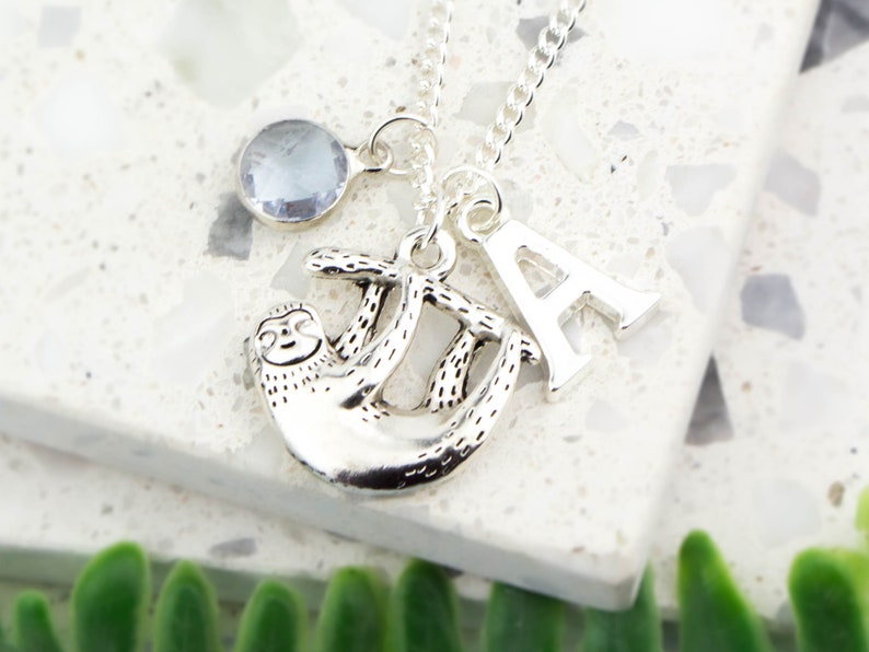May include: Silver necklace with a sloth charm, a crystal charm, and a letter A charm.