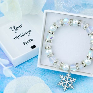 May include: A white bracelet with iridescent beads and a snowflake charm, in a white gift box with the text "Your message here".