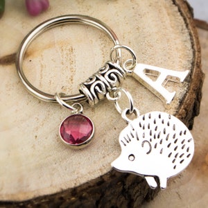 May include: Silver keychain with a pink crystal charm, a silver letter A charm, and a silver hedgehog charm.