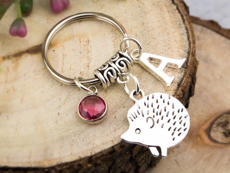 May include: Silver keychain with a pink crystal charm, a silver letter A charm, and a silver hedgehog charm.