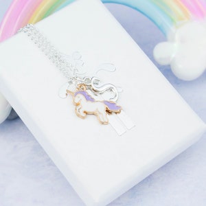 Op de afbeelding: Een zilveren ketting met een paarse en witte eenhoornbedel en een zilveren bedel. De ketting wordt gepresenteerd op een witte doos met een regenboogachtergrond.