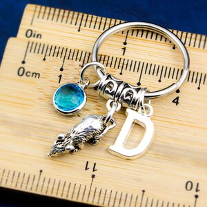 Puede incluir: Un llavero plateado con un dije de cristal azul, un dije de animal plateado y un dije plateado con la letra "D".