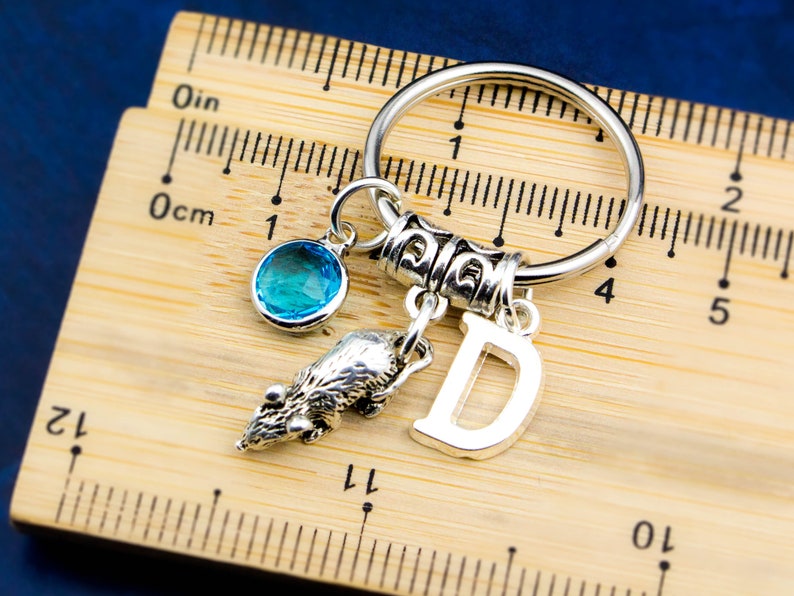 Puede incluir: Un llavero plateado con un dije de cristal azul, un dije de animal plateado y un dije plateado con la letra "D".