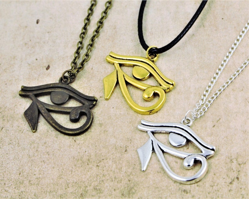 May include: Three necklaces with the Eye of Horus pendant. The pendants are made of silver, gold, and bronze. The necklaces are on a white background.