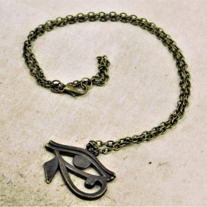 May include: A gold-toned necklace with a large, detailed Eye of Horus pendant. The chain is a double-link style.