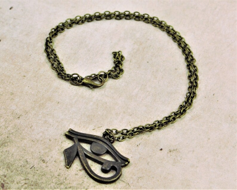 May include: A gold-toned necklace with a large, detailed Eye of Horus pendant. The chain is a double-link style.