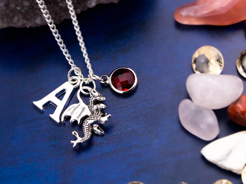 May include: Silver necklace with a silver letter A charm, a silver dragon charm, and a red gemstone charm.