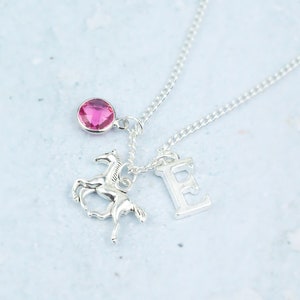 May include: Silver necklace with a pink gemstone, a silver horse charm, and a silver letter E charm.