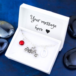May include: Silver charm necklace featuring a motorcycle charm, a red gemstone, and a silver charm with the number 0. The necklace is presented in a white gift box with the text "Your message here" and a heart.