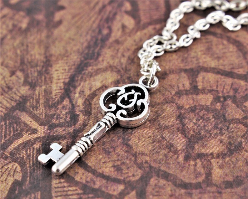 May include: A silver key necklace with a detailed, ornate key pendant. The key has a decorative, swirling design and a small, round bow at the top.