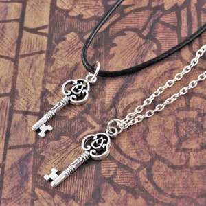 May include: Two silver key necklaces, one with a black cord and one with a silver chain. Both keys have ornate designs.