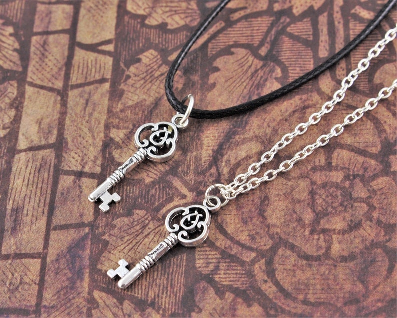 May include: Two silver key necklaces, one with a black cord and one with a silver chain. Both keys have ornate designs.