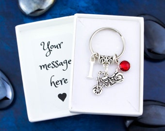 Puede incluir: Llavero de motocicleta plateado con un dije de cristal rojo y la letra "I" en un dije plateado. El llavero está en una caja de regalo blanca con una tarjeta en blanco que dice "Tu mensaje aquí".