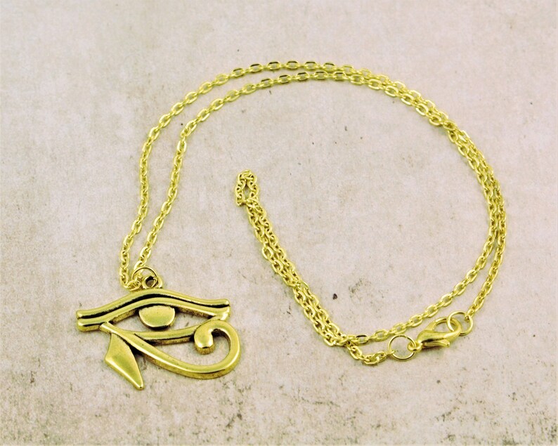 May include: A gold chain necklace with a gold pendant in the shape of the Eye of Horus.