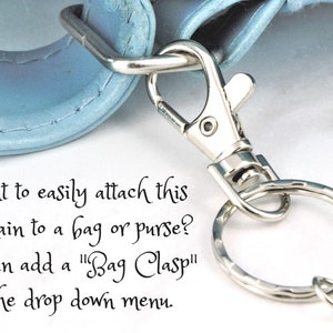 Puede incluir: Un llavero plateado con un cierre y un anillo. El texto "Want to easily attach this keychain to a bag or purse? You can add a "Bag Clasp" in the drop down menu." es visible en la imagen.