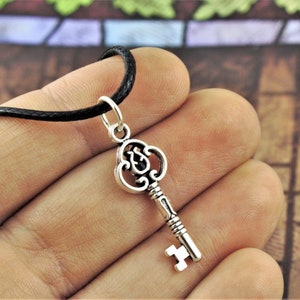 May include: A silver key pendant necklace with an ornate design. The key is attached to a black cord necklace.
