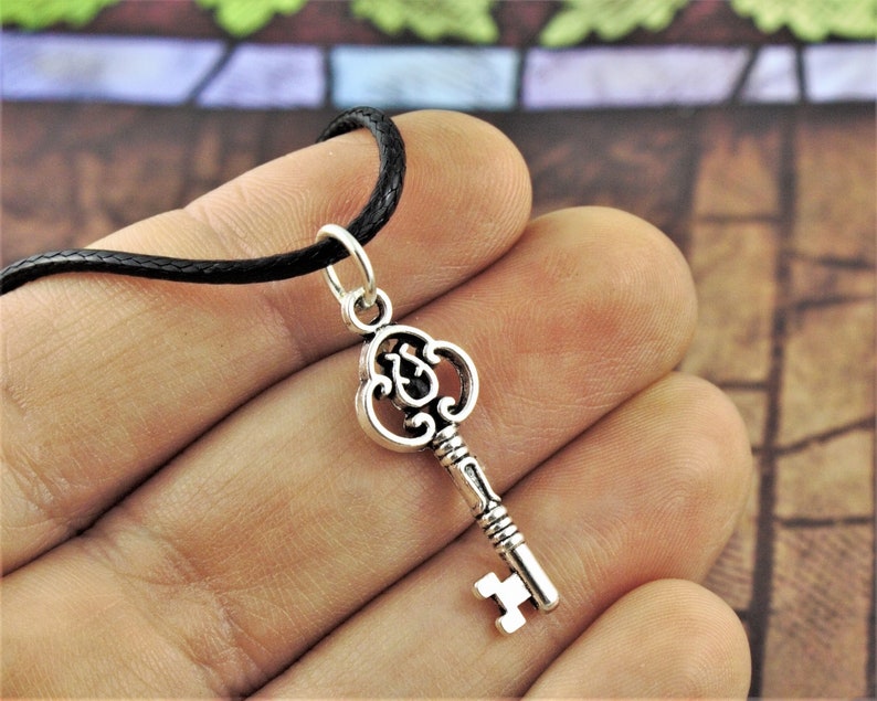 May include: A silver key pendant necklace with an ornate design. The key is attached to a black cord necklace.