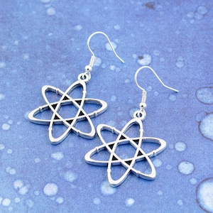 May include: A pair of silver earrings featuring an atom design. The earrings are displayed against a blue background.