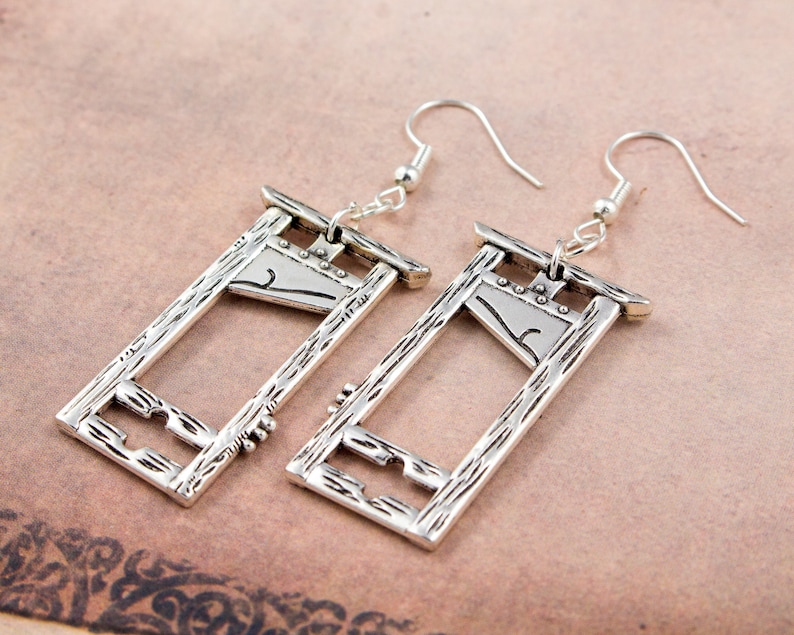 Puede incluir: Un par de pendientes de plata con forma de guillotina. Los pendientes tienen una superficie texturizada y est&aacute;n dise&ntilde;ados para parecer un instrumento de tortura medieval.