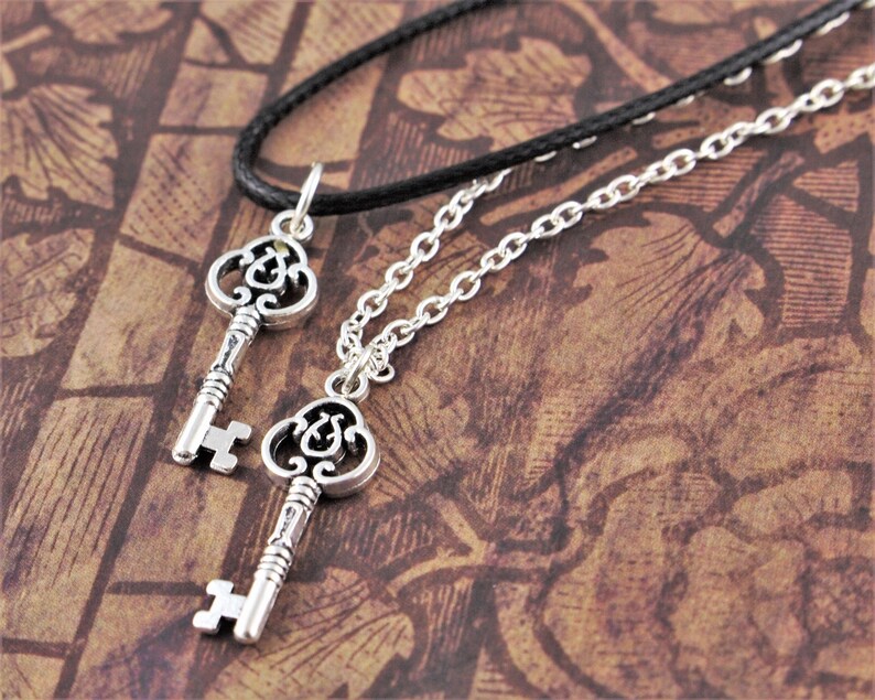 May include: Two silver key necklaces with intricate designs. One necklace has a black cord and the other has a silver chain.