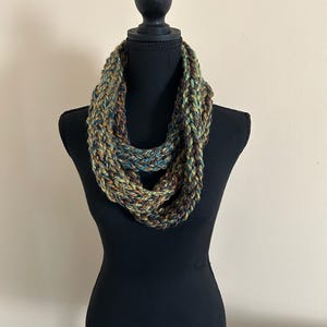 May include: A green, brown, and blue infinity scarf made of yarn. The scarf is displayed on a black mannequin.
